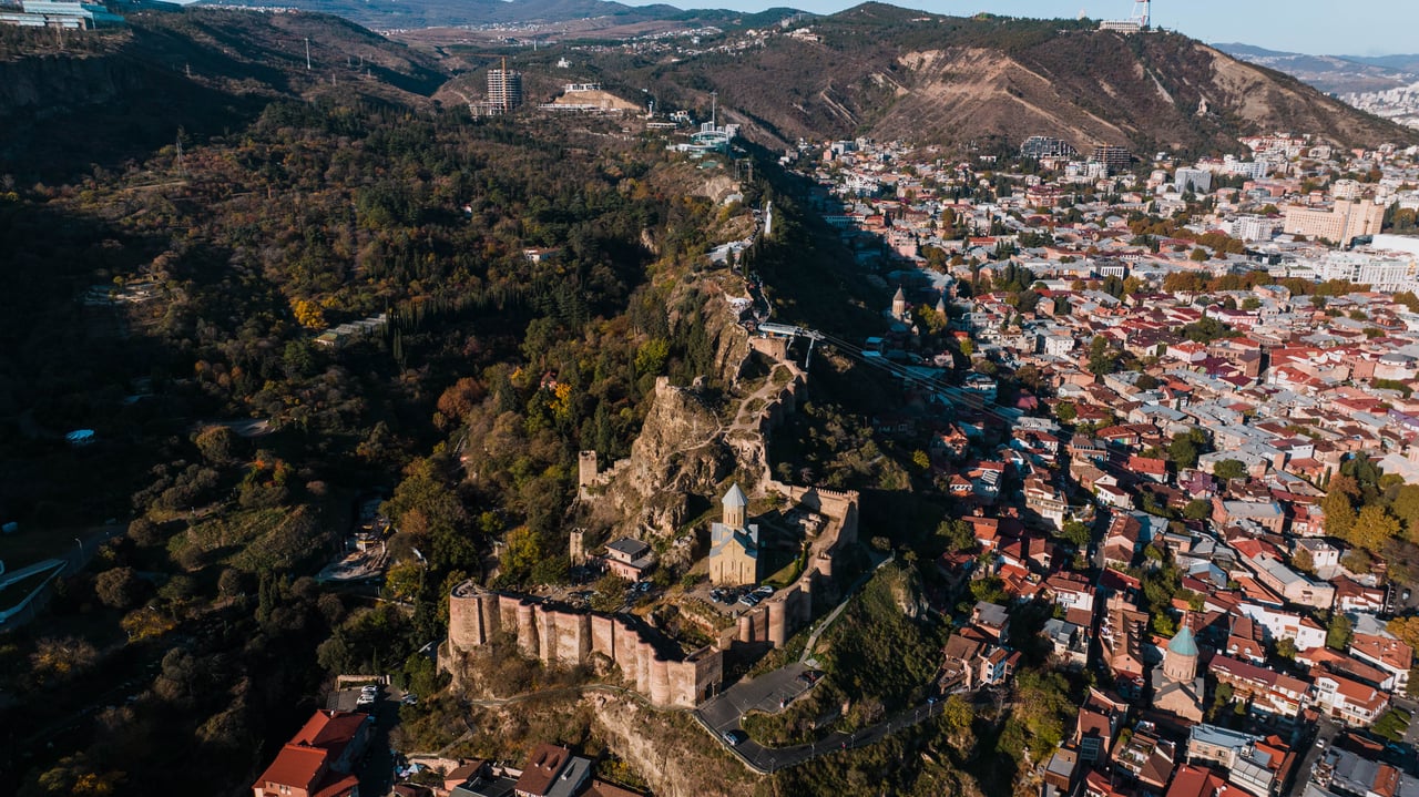 Stunning aerial shot of Narikala Fortress and Tbilisi cityscape showcasing historical architecture and vibrant urban life.