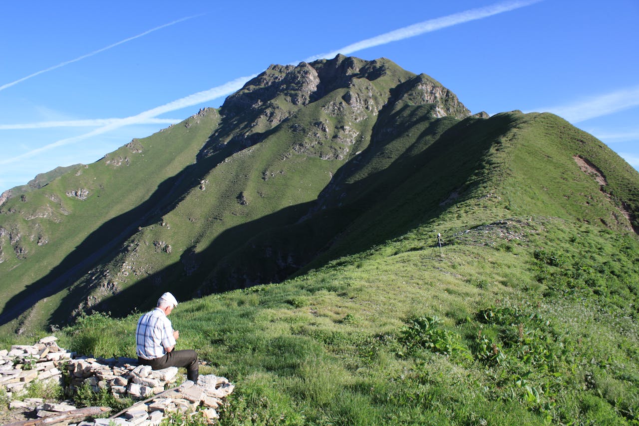 An elderly man enjoying a peaceful moment on a mountain trail under clear blue skies.